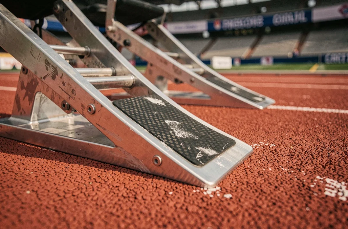 Gros plan sur des starting-blocks professionnels fixés sur une piste d'athlétisme en tartan rouge avec détails mécaniques