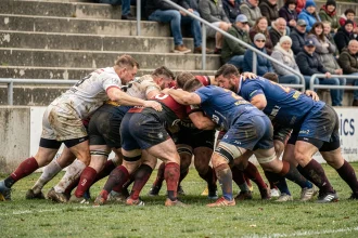 Mêlée serrée lors d'un match de rugby Nationale 2, joueurs en tenue de club en plein effort collectif sur pelouse