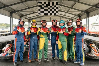 Groupe d'employés en combinaisons de karting posant ensemble dans le stand d'un circuit indoor lors d'un team building d'entreprise à Niort